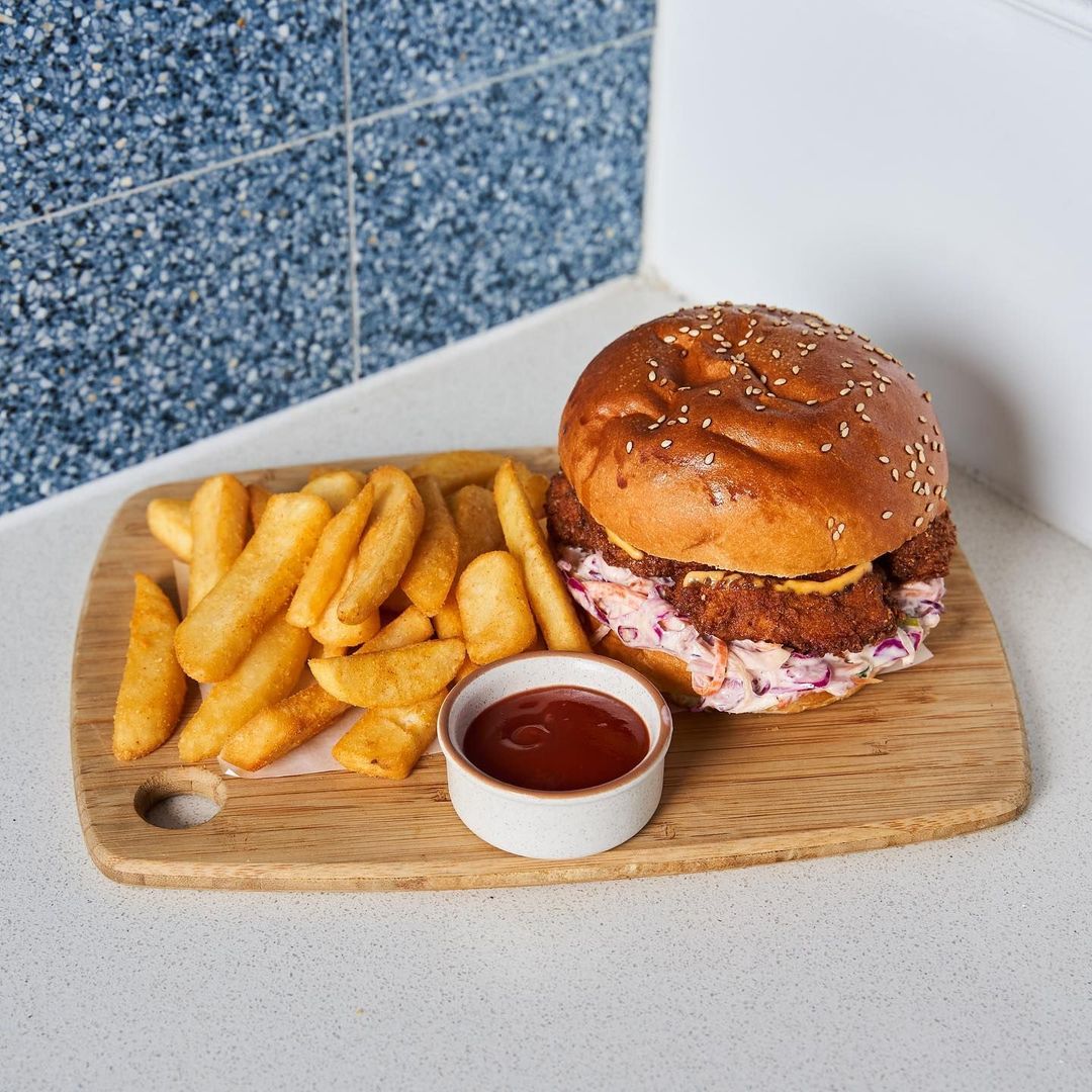 A crispy chicken and slaw burger on a sesame bun with chips and tomato sauce