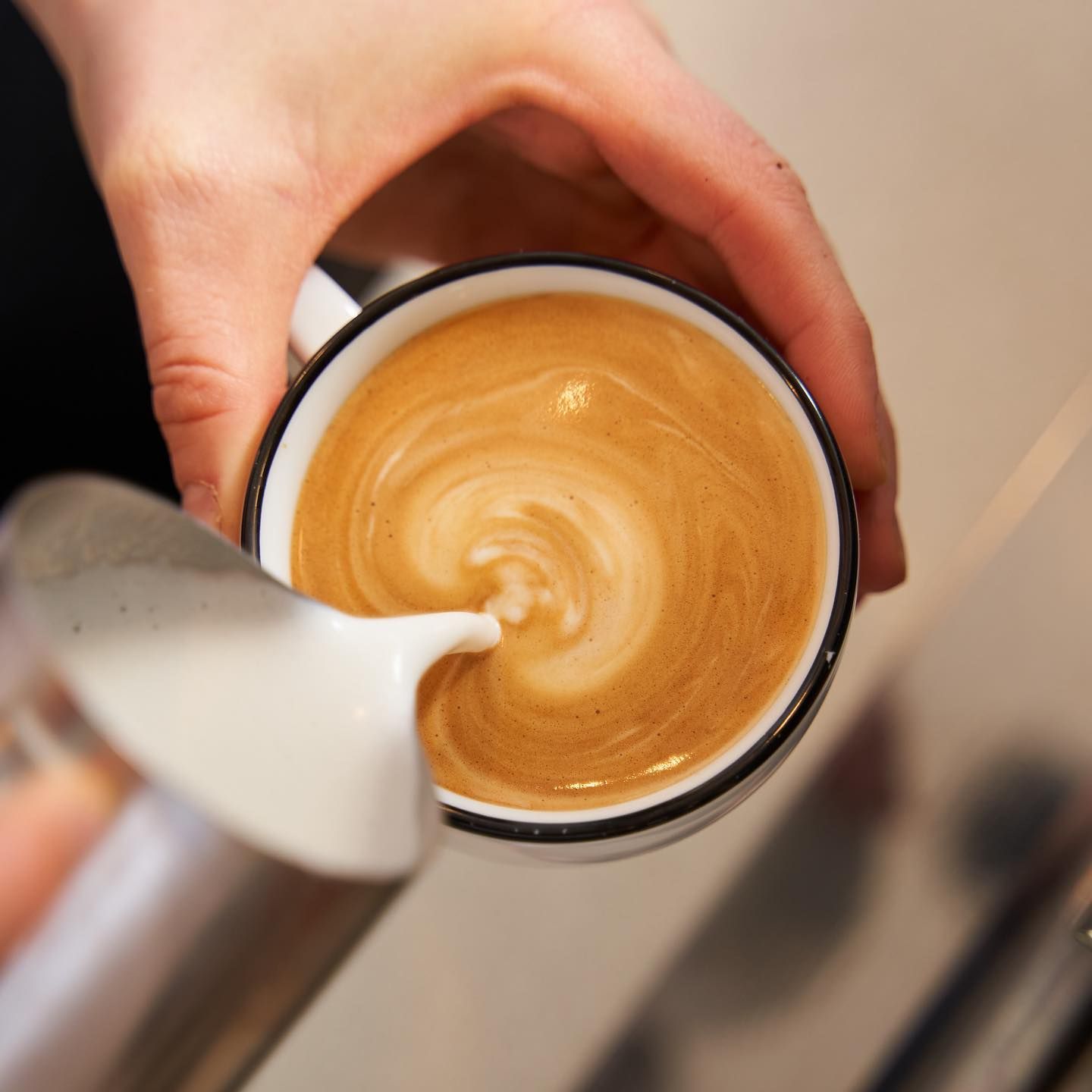 A Drip Cafe barista pouring milk to finish latte art