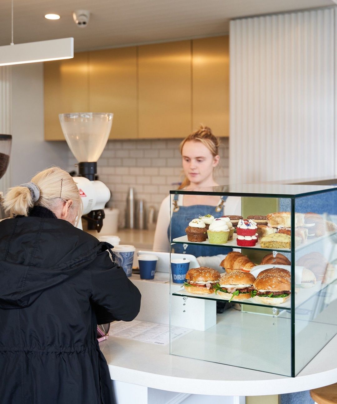A customer ordering at the Drip Cafe counter beside the pastry cabinet